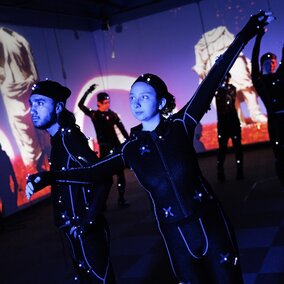 Fine and performing arts students perform in lighted costumes.